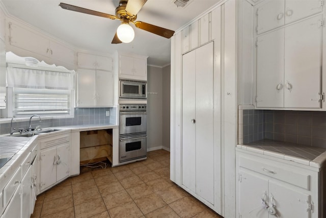 kitchen featuring a sink, appliances with stainless steel finishes, white cabinetry, and tile counters