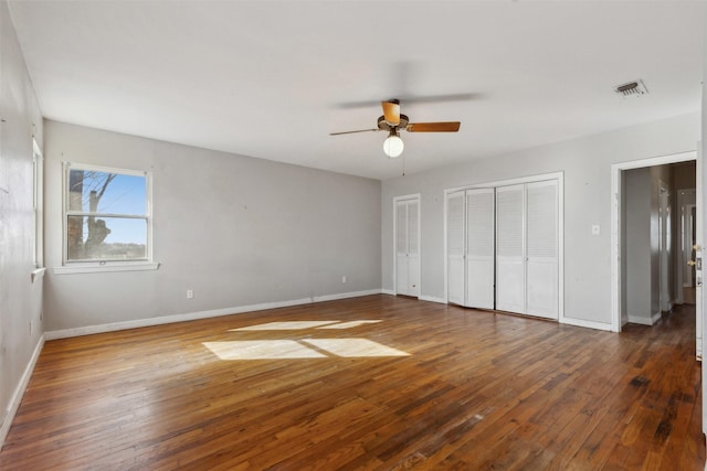 unfurnished bedroom with hardwood / wood-style flooring, baseboards, visible vents, and two closets