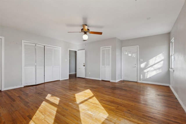 unfurnished bedroom featuring baseboards, two closets, a ceiling fan, and hardwood / wood-style flooring