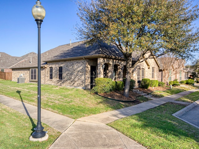 view of front of house featuring a front yard, central air condition unit, brick siding, and roof with shingles