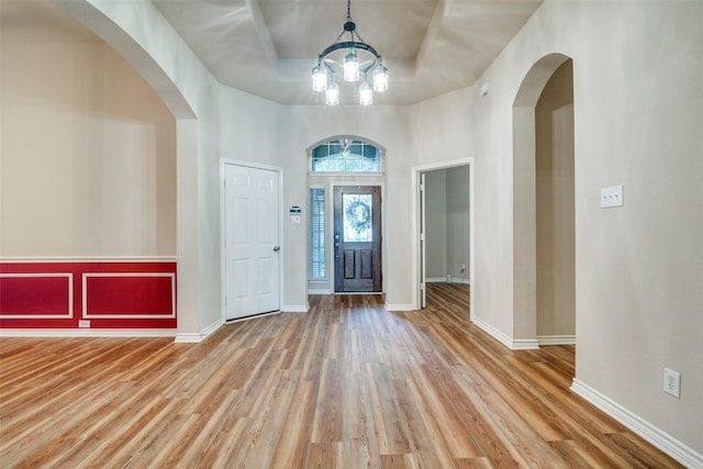 entrance foyer with a tray ceiling, arched walkways, baseboards, and wood finished floors