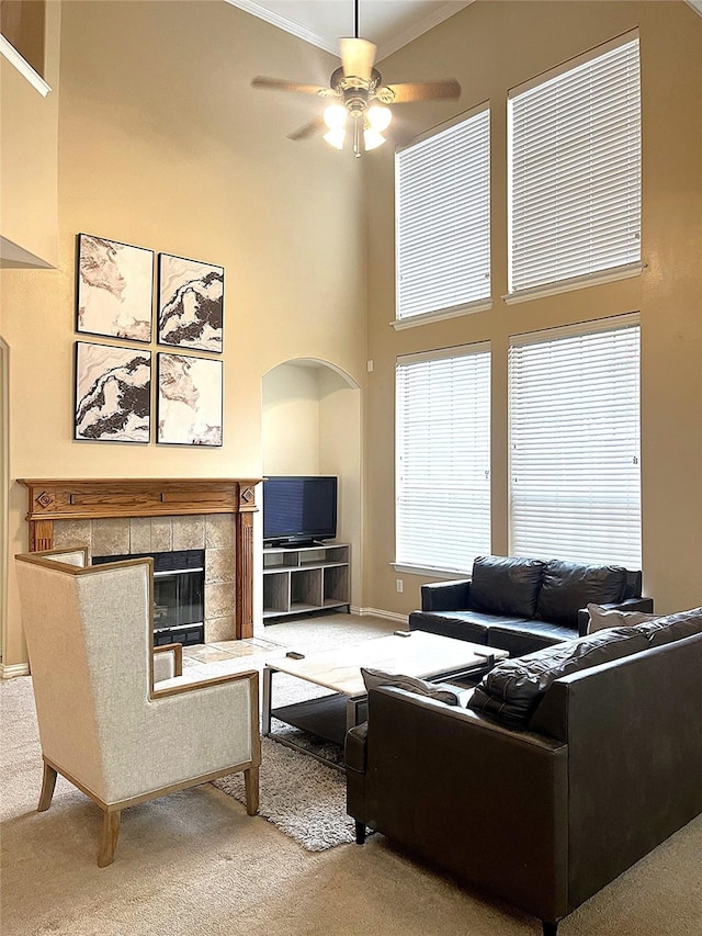 carpeted living area featuring ornamental molding, a ceiling fan, a fireplace, baseboards, and a towering ceiling