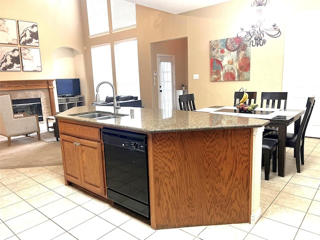 kitchen with a sink, black dishwasher, a tiled fireplace, and light tile patterned floors