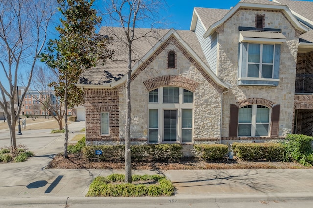 french country inspired facade featuring brick siding, stone siding, and a shingled roof