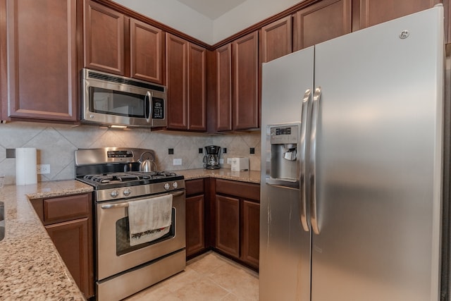 kitchen with light tile patterned floors, stainless steel appliances, light stone countertops, and tasteful backsplash