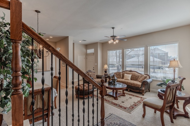 carpeted living area featuring baseboards, a ceiling fan, a healthy amount of sunlight, and stairs