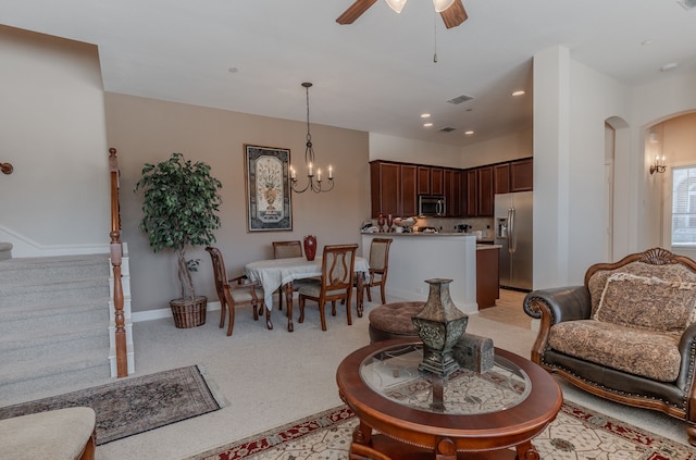 living area featuring arched walkways, stairway, ceiling fan with notable chandelier, and light colored carpet