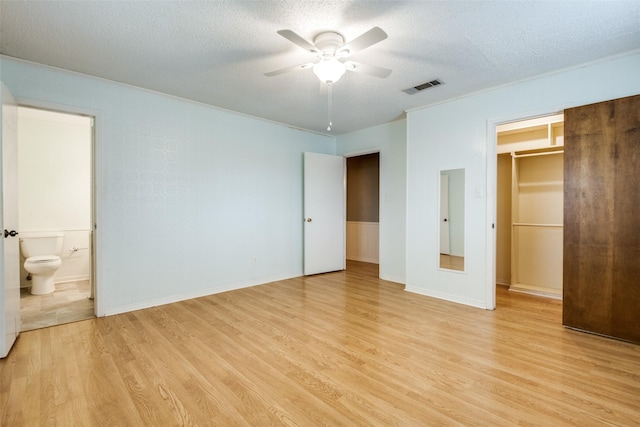 unfurnished bedroom featuring a textured ceiling, a spacious closet, light wood-type flooring, and visible vents