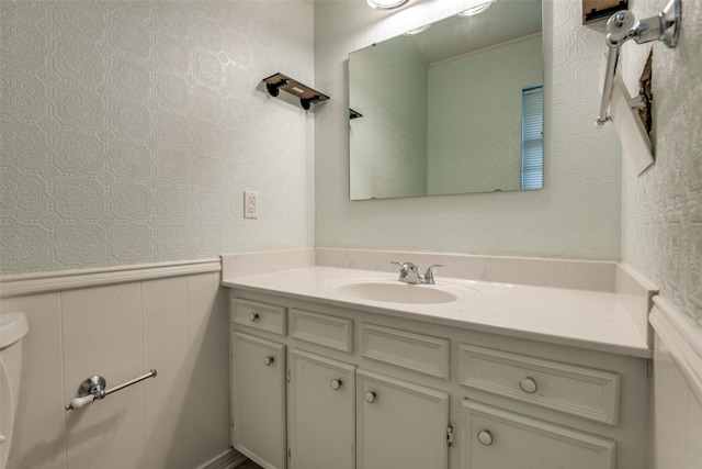 bathroom featuring toilet, a wainscoted wall, a decorative wall, and vanity