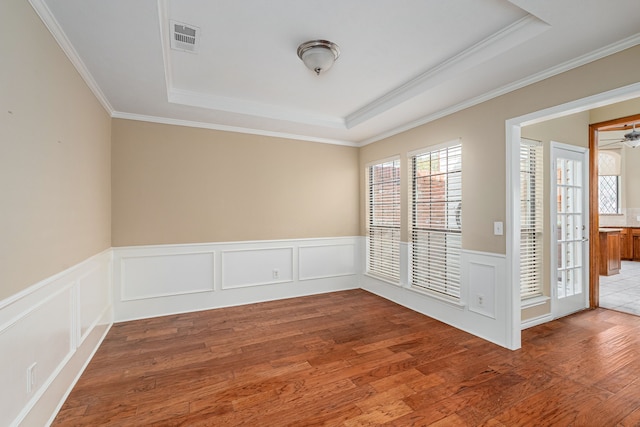 unfurnished room with visible vents, a tray ceiling, wood finished floors, and wainscoting