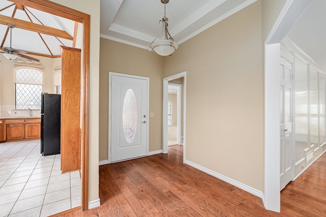 foyer with baseboards, a ceiling fan, a tray ceiling, crown molding, and light wood-style floors