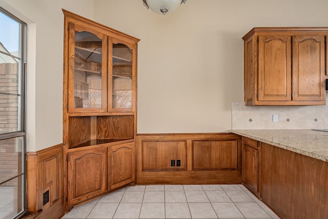 kitchen with brown cabinets, wainscoting, light tile patterned flooring, and light stone counters