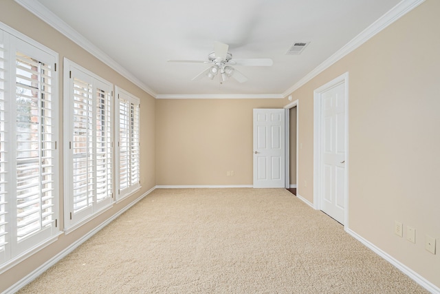 spare room featuring carpet, crown molding, visible vents, ceiling fan, and baseboards