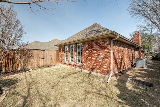 view of side of home featuring central AC, brick siding, fence, a yard, and a chimney