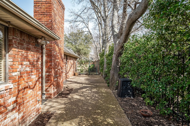 view of side of home with a chimney, fence, and brick siding