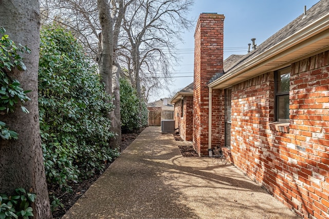 view of home's exterior with brick siding, a chimney, central AC unit, a patio area, and fence