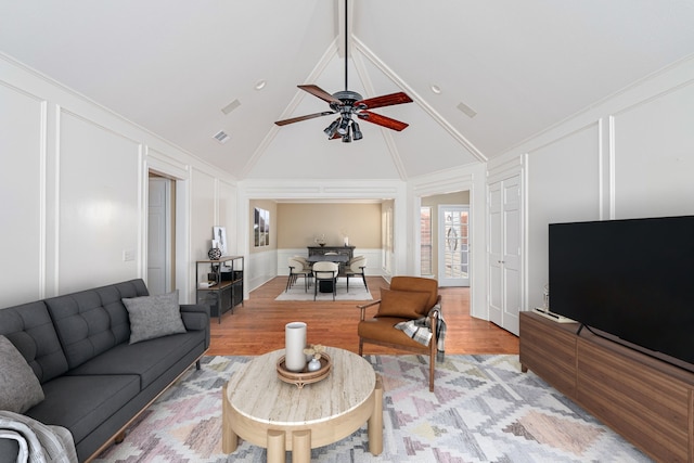 living area with light wood-type flooring, high vaulted ceiling, a decorative wall, and a ceiling fan