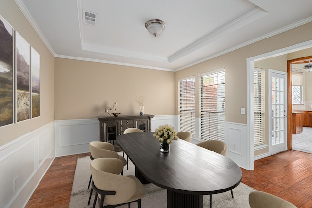 dining space featuring a wainscoted wall, wood finished floors, and a raised ceiling