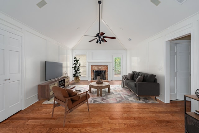 living room with ceiling fan, a decorative wall, a fireplace, wood finished floors, and visible vents