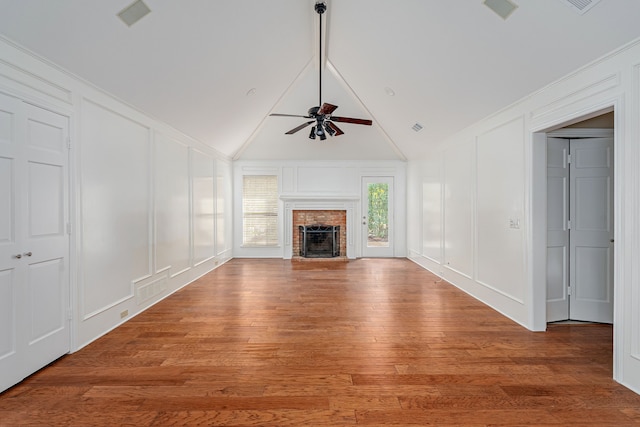 unfurnished living room featuring a ceiling fan, a brick fireplace, a decorative wall, and light wood finished floors