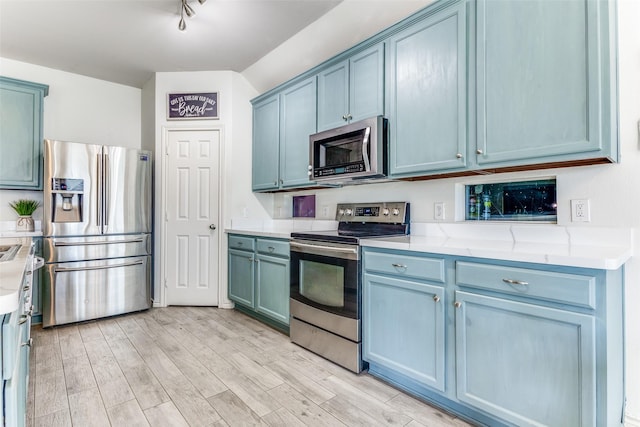 kitchen with blue cabinetry, rail lighting, stainless steel appliances, and light wood-type flooring