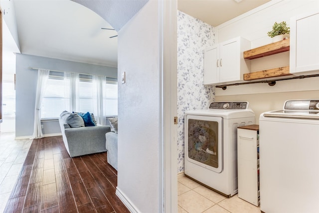 washroom featuring wood finished floors, cabinet space, arched walkways, wallpapered walls, and washing machine and clothes dryer