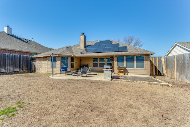 rear view of house featuring roof mounted solar panels, a patio area, a fenced backyard, and a chimney