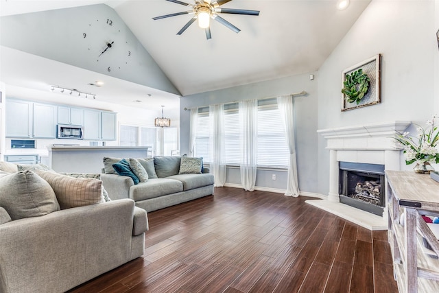 living area featuring a fireplace with raised hearth, dark wood-type flooring, baseboards, ceiling fan, and high vaulted ceiling