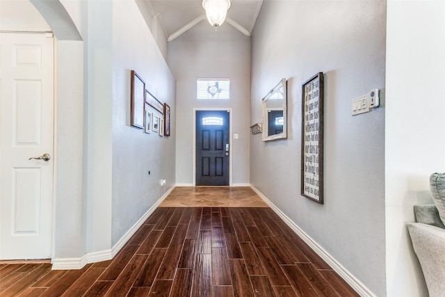 entryway featuring baseboards, lofted ceiling, arched walkways, dark wood-type flooring, and crown molding