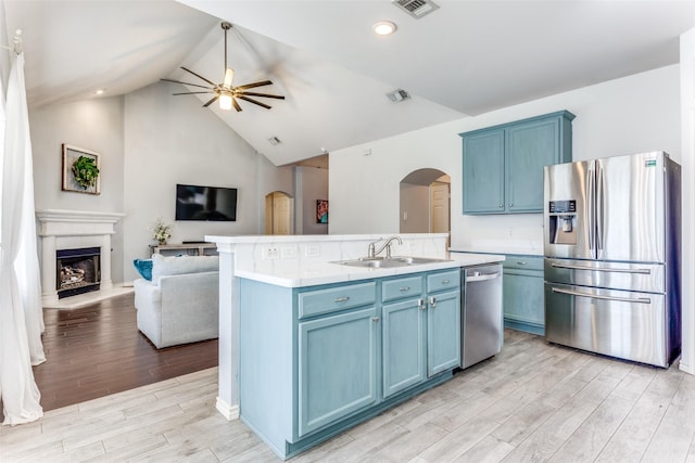 kitchen with a ceiling fan, a sink, appliances with stainless steel finishes, blue cabinets, and open floor plan