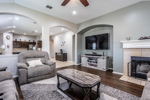 living room featuring lofted ceiling, a tile fireplace, recessed lighting, wood finished floors, and visible vents