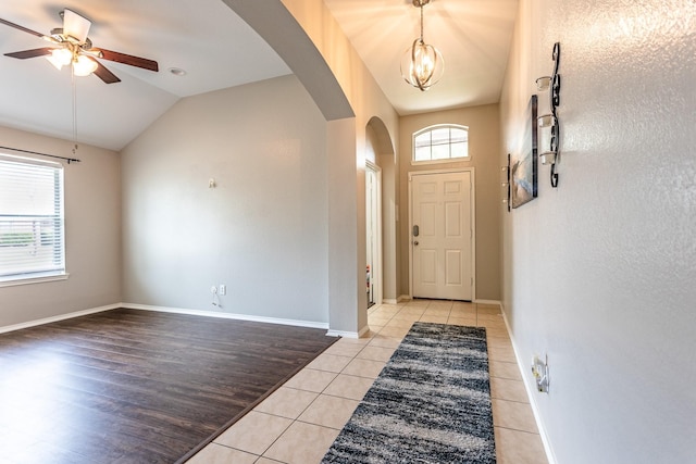 foyer featuring arched walkways, lofted ceiling, light tile patterned flooring, ceiling fan with notable chandelier, and baseboards