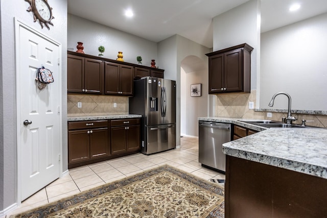 kitchen featuring arched walkways, appliances with stainless steel finishes, a sink, and dark brown cabinetry