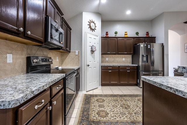 kitchen with arched walkways, light tile patterned floors, light countertops, appliances with stainless steel finishes, and dark brown cabinets