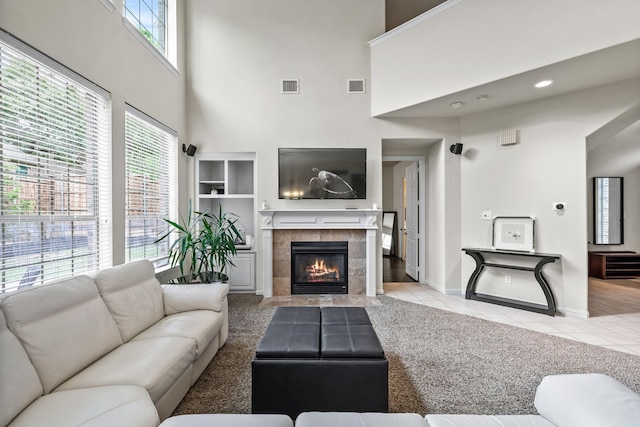 tiled living area with baseboards, visible vents, a fireplace, and a high ceiling