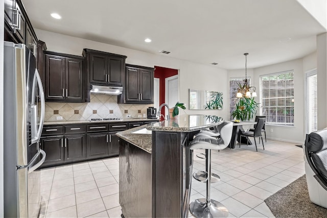 kitchen featuring a breakfast bar area, light tile patterned floors, decorative backsplash, appliances with stainless steel finishes, and under cabinet range hood