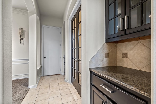 kitchen featuring light tile patterned floors, decorative backsplash, glass insert cabinets, dark stone counters, and baseboards