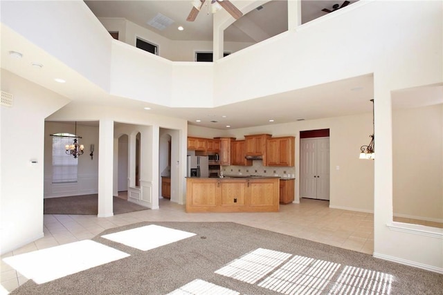 unfurnished living room featuring light tile patterned floors, a high ceiling, ceiling fan with notable chandelier, and light colored carpet