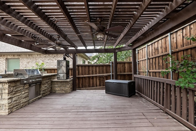 deck with an outdoor kitchen, area for grilling, ceiling fan, fence, and a pergola