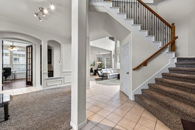 entrance foyer with ornamental molding, light carpet, ceiling fan, and light tile patterned floors