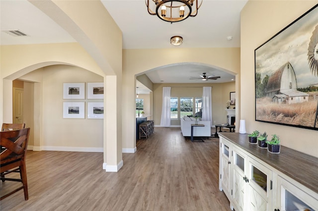 foyer featuring light wood-style floors, baseboards, arched walkways, and a ceiling fan