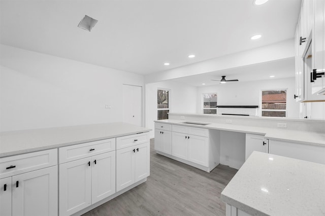 kitchen featuring a peninsula, light stone countertops, light wood-type flooring, and white cabinetry