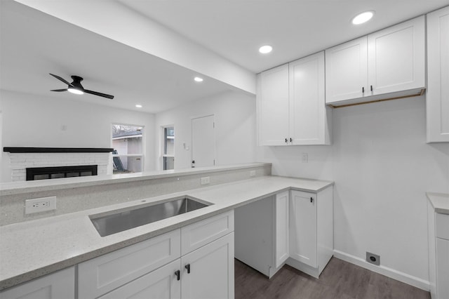 kitchen featuring dark wood-type flooring, a fireplace, a sink, and white cabinets