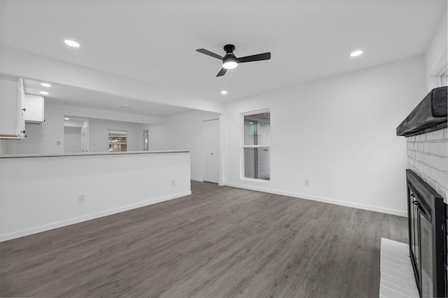 unfurnished living room featuring dark wood-type flooring, recessed lighting, a fireplace, and baseboards