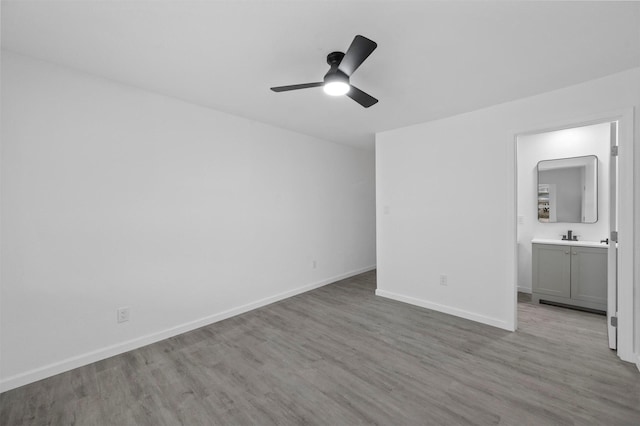 unfurnished bedroom featuring ensuite bath, wood finished floors, a ceiling fan, and baseboards