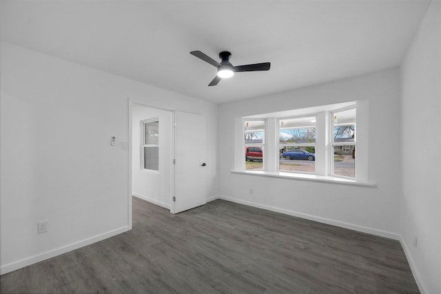 spare room with dark wood finished floors, a ceiling fan, and baseboards