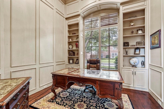 office space with built in shelves, a decorative wall, and dark wood-style floors