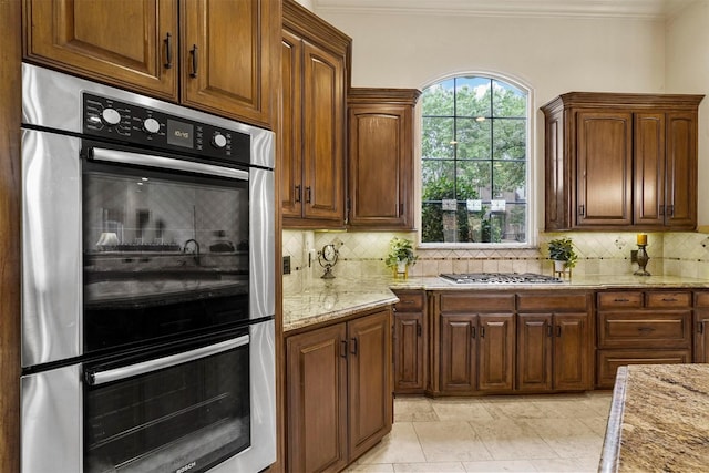 kitchen with appliances with stainless steel finishes, crown molding, light stone counters, and tasteful backsplash