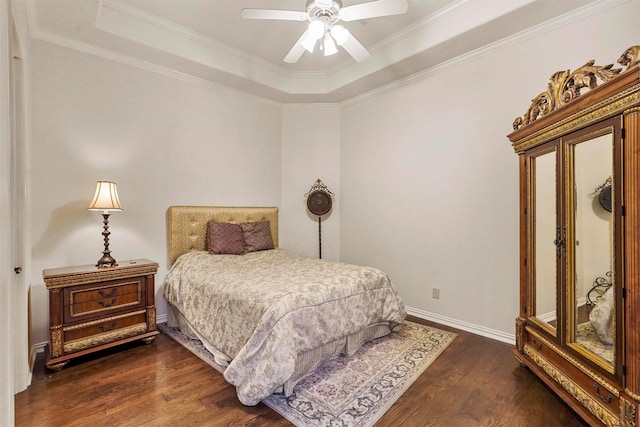 bedroom with a tray ceiling, dark wood-style flooring, crown molding, and baseboards