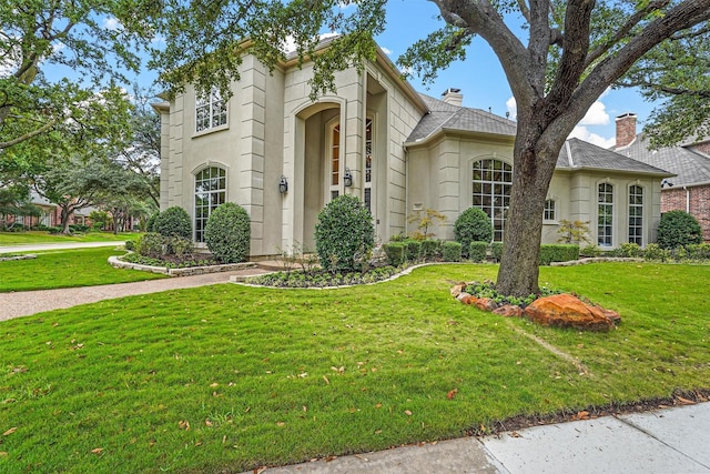 mediterranean / spanish house featuring stucco siding, a chimney, and a front yard